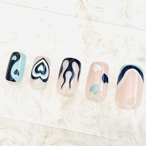 May include: Five nude-colored press-on nails with different abstract designs. The designs include a yin-yang symbol, a heart, flames, a swirl, and a cloud.