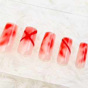 Könnte beinhalten: Satz mit sechs falschen Nägeln mit einem rot-weißen Ombre-Design. Einige Nägel haben ein rotes X-Design.