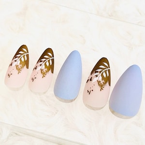 May include: Five long, almond-shaped false nails with a light blue and light pink ombre design. The nails have a gold leaf design on the pink portion.