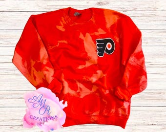 May include: Red sweatshirt with a white tie-dye pattern and a black and orange Philadelphia Flyers logo.