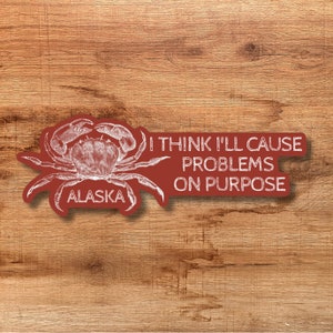 May include: Red sticker with a white outline of a crab and the text "I think I'll cause problems on purpose" and "Alaska" below the crab.