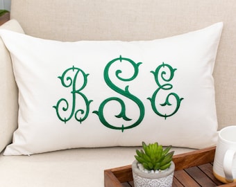 May include: A white pillow with green embroidered letters "BSE" on a cream colored couch with a wooden tray and a small potted succulent plant.