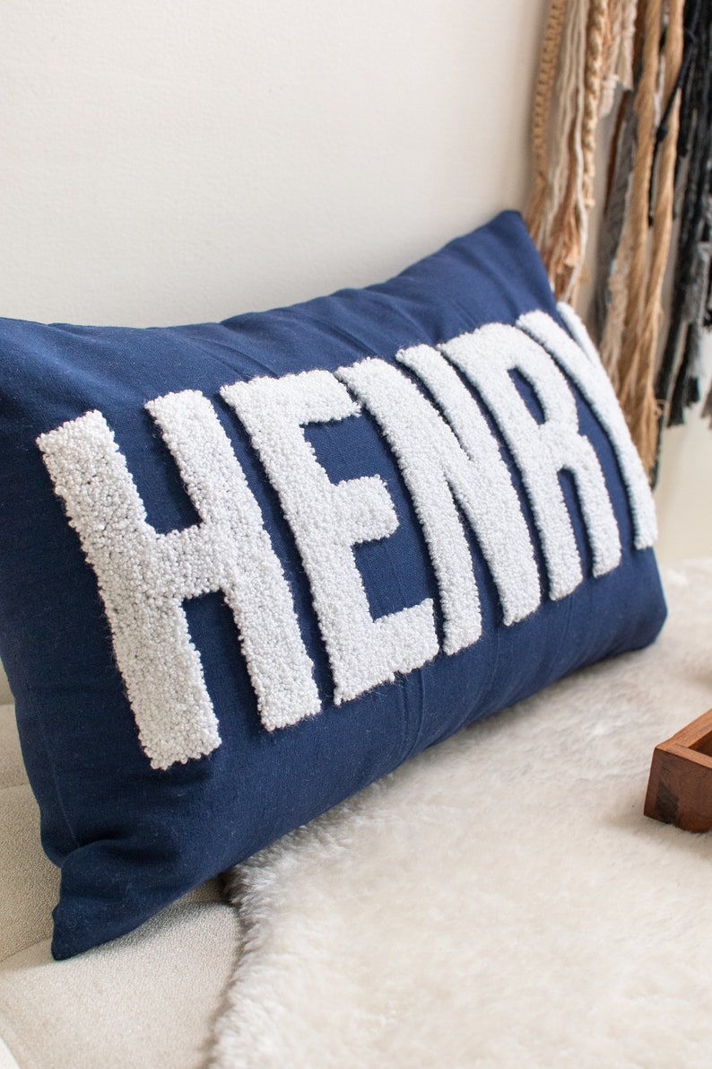 May include: A blue pillow with the name "HENRY" spelled out in white fluffy letters.