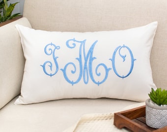 May include: A white throw pillow with a blue embroidered monogram "JMO" on a white couch.