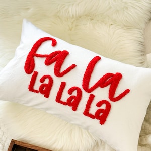 May include: White throw pillow with red embroidered text that reads "fa la la la".