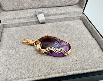 May include: A purple and brown agate gemstone pendant wrapped in gold wire.