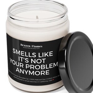 Puede incluir: Una vela blanca en un tarro de cristal transparente con una etiqueta negra. La etiqueta dice "Smells Like It's Not Your Problem Anymore". La tapa negra est&aacute; al lado del tarro. La vela est&aacute; vertida a mano en California.