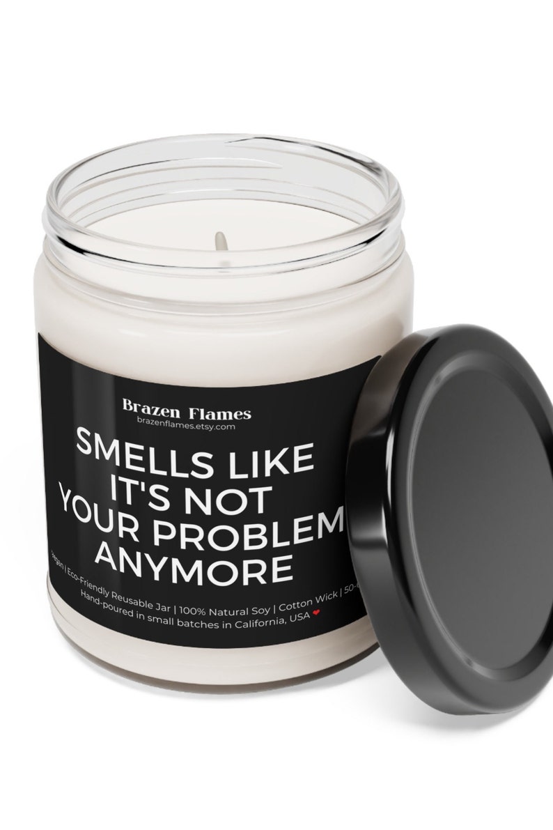 Puede incluir: Una vela blanca en un tarro de cristal transparente con una etiqueta negra. La etiqueta dice "Smells Like It's Not Your Problem Anymore". La tapa negra est&aacute; al lado del tarro. La vela est&aacute; vertida a mano en California.