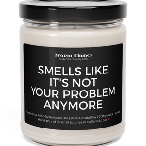 Puede incluir: Vela en tarro de cristal transparente con tapa negra y etiqueta negra. La etiqueta dice "SMELLS LIKE IT'S NOT YOUR PROBLEM ANYMORE" en texto blanco. La vela est&aacute; hecha con cera de soja natural y una mecha de algod&oacute;n.