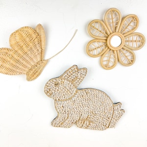 May include: Three wall decor pieces made of natural materials. A woven butterfly, a woven rabbit, and a woven flower with a mirror in the centre.