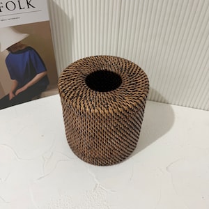 K&ouml;nnte beinhalten: Ein runder, geflochtener Wicker-Gewebe-Tischtuchhalter in dunkelbrauner Farbe.