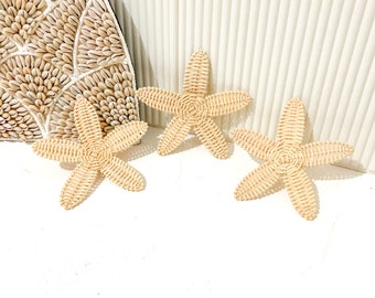 Puede incluir: Tres decoraciones de pared de estrella de mar tejidas en color beige claro. Las estrellas de mar están hechas de materiales naturales y tienen un aspecto rústico y playero.