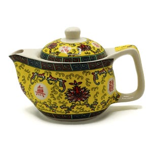 Op de afbeelding: Gele keramische theepot met deksel, tuit en handvat. De theepot is versierd met rode en gele bloemmotieven en Chinese karakters. De handgreep en de knop van het deksel zijn gebroken wit.