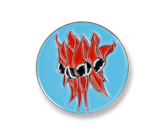 May include: A round enamel pin featuring a stylized floral design. The pin has a light blue background with a silver border. The floral design is red with black accents. The pin is likely a decorative accessory.
