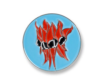 May include: A round enamel pin featuring a stylized floral design. The pin has a light blue background with a silver border. The floral design is red with black accents. The pin is likely a decorative accessory.