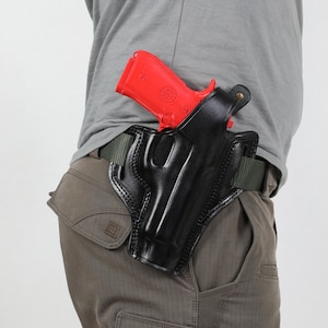 Op de afbeelding: Een zwart leren holster met een rood pistool erin. Het holster wordt gedragen op een riem.