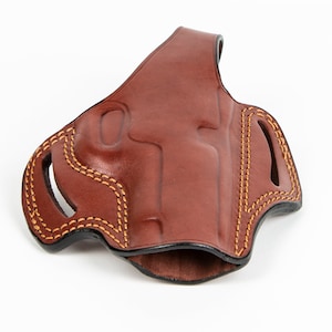 Könnte beinhalten: Ein braunes Lederholster mit einem genähten Design und einem Ausschnitt für eine Pistole.