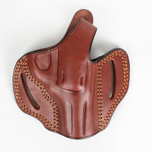 Puede incluir: Una funda de cuero marrón con un diseño cosido. La funda tiene un bucle para el cinturón y una solapa para asegurar el arma de fuego.
