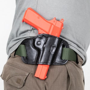 Op de afbeelding: Een zwart leren holster met een rood plastic pistool erin. Het holster is bevestigd aan een groene riem.
