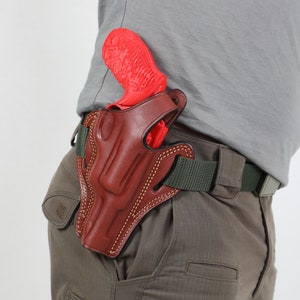 May include: A brown leather holster with a red gun inside. The holster is attached to a green belt.