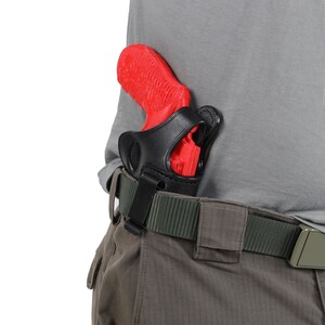 May include: A red handgun in a black leather holster attached to a green belt. The holster is secured to the belt with a black clip.