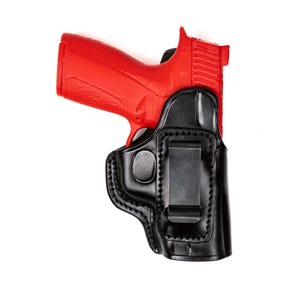 Peut inclure: Un pistolet rouge est partiellement inséré dans un étui en cuir noir. L'étui a un clip métallique à l'arrière pour la fixation. Les coutures de l'étui sont visibles, et le fond est blanc.