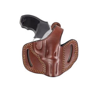 May include: A brown leather holster with a stitched design, holding a black and silver handgun. The holster has a curved shape with openings for the barrel and trigger. The handgun's grip is visible.