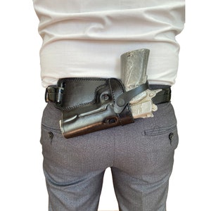 Könnte beinhalten: Ein schwarzes Lederholster mit einer silbernen Pistole darin. Das Holster ist an einem schwarzen Gürtel befestigt, der um die Taille getragen wird.