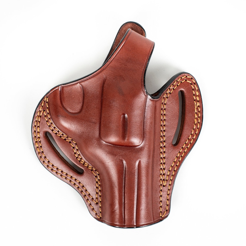 May include: A brown leather holster with a stitched design. The holster has a flap that covers the top of the gun.