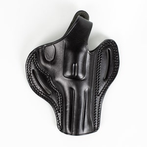 Op de afbeelding: Een zwart leren holster met ingewikkelde stiksels en een gevormd ontwerp. Het holster heeft een riemlus en is ontworpen om een vuurwapen veilig vast te houden. Het algehele ontwerp is strak en functioneel.