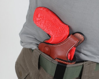 Könnte beinhalten: Eine rote Pistole in einem braunen Lederholster mit einem schwarzen Clip, der an einem grünen Gürtel befestigt ist.