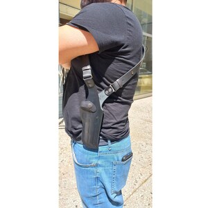 Op de afbeelding: Zwart leren schouderholster met een riem en een wapencompartiment. Het holster wordt over de schouder en onder de arm gedragen. Het holster is ontworpen om een ​​handvuurwapen te bevatten. Het holster is gemaakt van leer en heeft een knoopsluiting.
