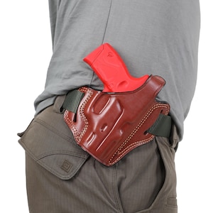 Puede incluir: Una funda de cuero marrón con una pistola roja en su interior. La funda está unida a un cinturón verde y se lleva en la cintura.