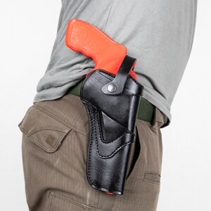 Op de afbeelding: Een zwart leren holster met een rood en oranje pistool erin. Het holster wordt gedragen op een riem.
