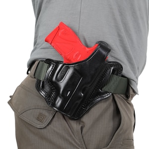 Könnte beinhalten: Ein schwarzes Lederholster mit einer roten Plastikpistole darin. Das Holster ist an einem grünen Gürtel befestigt.