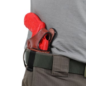 Op de afbeelding: Een rood pistool in een bruine leren holster bevestigd aan een groene en bruine riem.