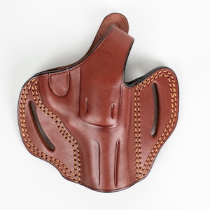 Op de afbeelding: Een bruine leren holster met stikseldetails. De holster heeft een riemlus en een trekkerbescherming.