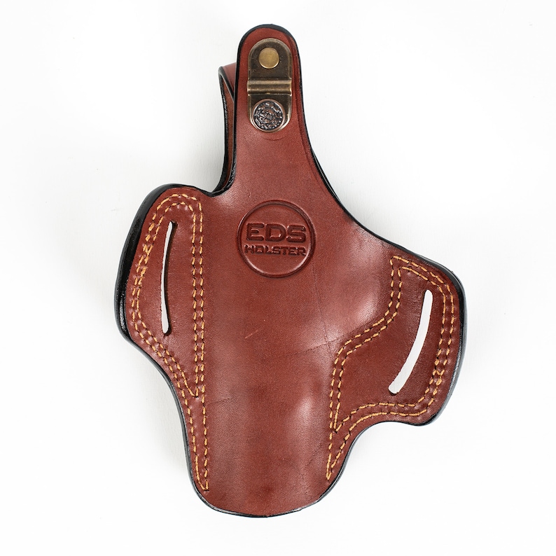 May include: Brown leather holster with a black stitching detail and a brass snap closure. The holster has the text "EDS HOLSTER" embossed on the front.