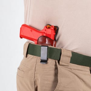 Peut inclure: Un pistolet rouge dans un étui en cuir marron attaché à une ceinture verte. L'étui est doté d'un clip métallique qui se fixe à la ceinture.