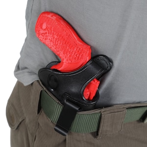 Op de afbeelding: Een rood pistool in een zwart leren holster bevestigd aan een groene riem. Het holster is met een zwarte clip aan de riem bevestigd.