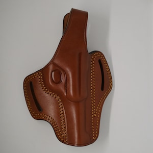 May include: A brown leather holster with a stitched design and a belt loop.
