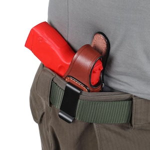 May include: A brown leather holster with a black clip attached to a green belt. A red plastic gun is inside the holster.
