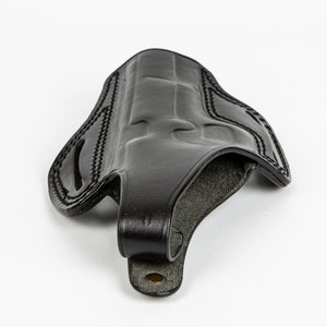 May include: A black leather holster with a stitched design and a belt loop.