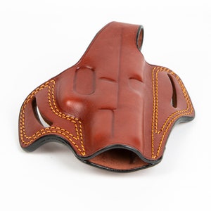 Könnte beinhalten: Ein braunes Lederholster mit einem genähten Design und einem schwarzen Futter. Das Holster ist für eine Pistole ausgelegt.