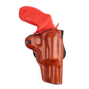 May include: A brown leather holster with a red handgun. The holster is designed to securely hold the firearm. The image is set against a white background, highlighting the details of the leather and the gun.