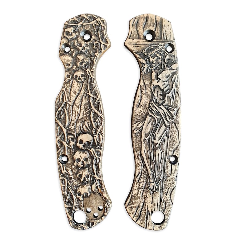 May include: Two knife scales with intricate carvings. One scale features a skull and crossbones design with thorns, while the other depicts a figure of Jesus Christ on the cross.