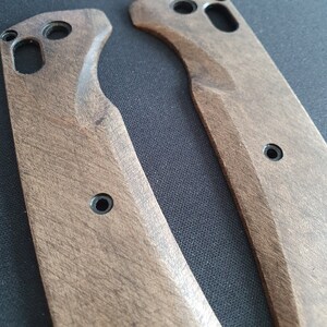 Op de afbeelding: Twee onafgewerkte houten meshandvatten met een donkerbruine vlek. De handvatten hebben een gebogen vorm en zijn gemaakt van glad hout.