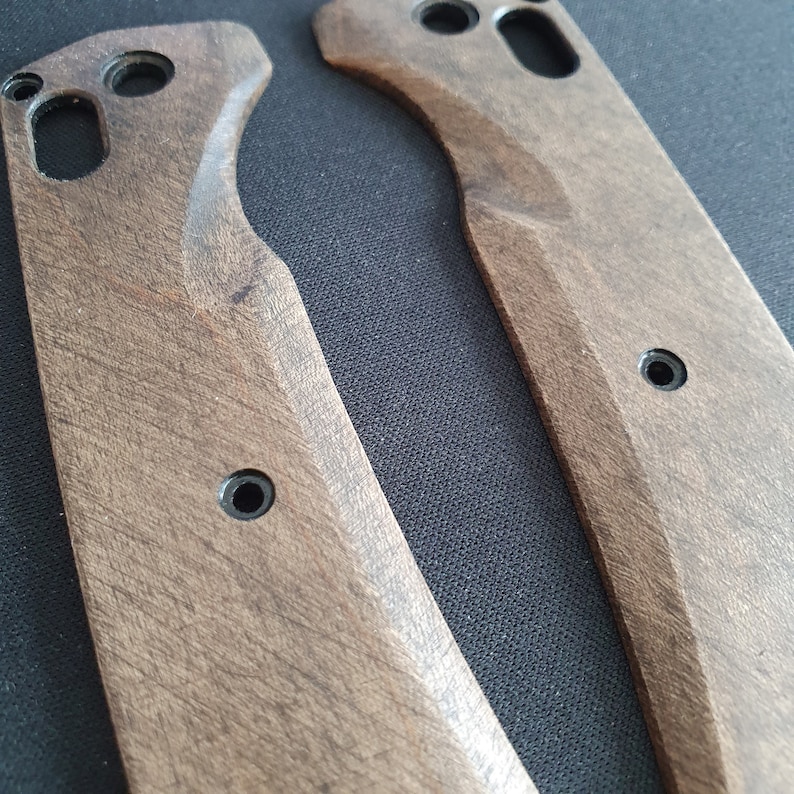 Op de afbeelding: Twee onafgewerkte houten meshandvatten met een donkerbruine vlek. De handvatten hebben een gebogen vorm en zijn gemaakt van glad hout.