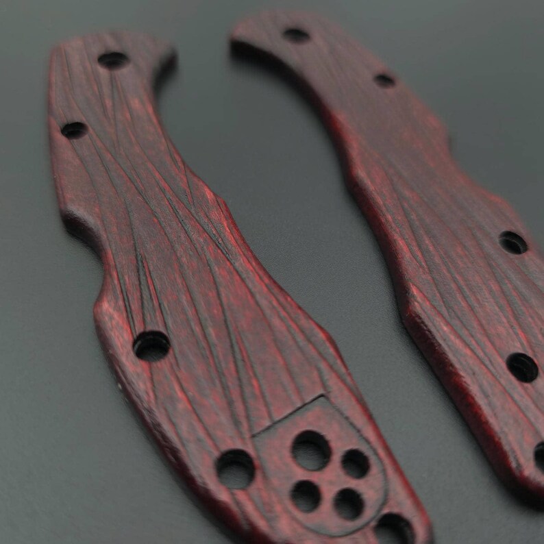 Puede incluir: Dos cachas de mango de cuchillo rojas y negras con textura de vetas de madera. Cada cacha tiene m&uacute;ltiples agujeros para tornillos y una forma curva para un agarre c&oacute;modo. Las cachas est&aacute;n dise&ntilde;adas para una navaja plegable.