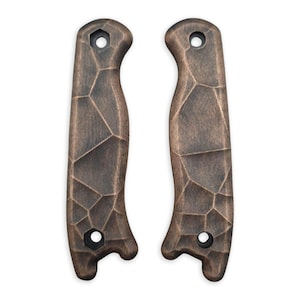 May include: Two bronze-colored knife handle scales with a geometric, textured pattern. Each scale has a curved shape with a hole at each end for attachment. The scales are designed for a knife and are displayed against a white background.